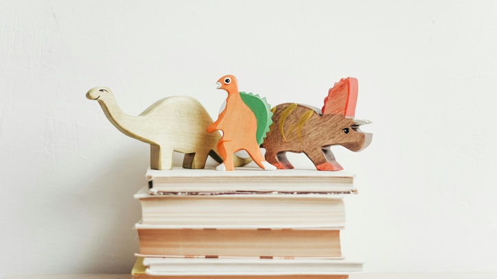 Drei Spielzeugdinosaurier stehen auf einem Stapel Bücher
