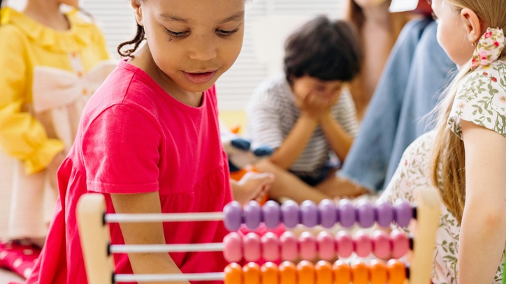 Eine Gruppe von Kindern. Im Vordergrund ist ein Rechenschieber im Hintergrund eine Betreuerin zu sehen.