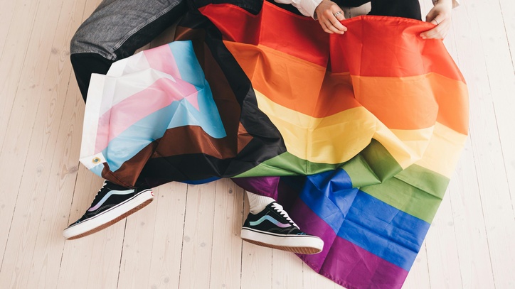 Zwei Personen sitzen mit einer Trans-Pride und einer Regenbogenflagge auf dem Boden