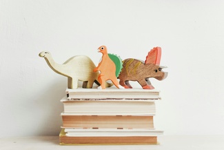 Drei Spielzeugdinosaurier stehen auf einem Stapel Bücher