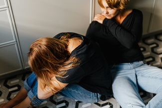 Zwei Frauen sitzen auf dem Boden. Die eine tröstet die andere Frau.