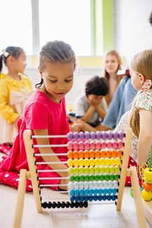 Eine Gruppe von Kindern. Im Vordergrund ist ein Rechenschieber im Hintergrund eine Betreuerin zu sehen.