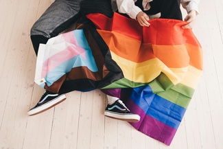 Zwei Personen sitzen mit einer Trans-Pride und einer Regenbogenflagge auf dem Boden